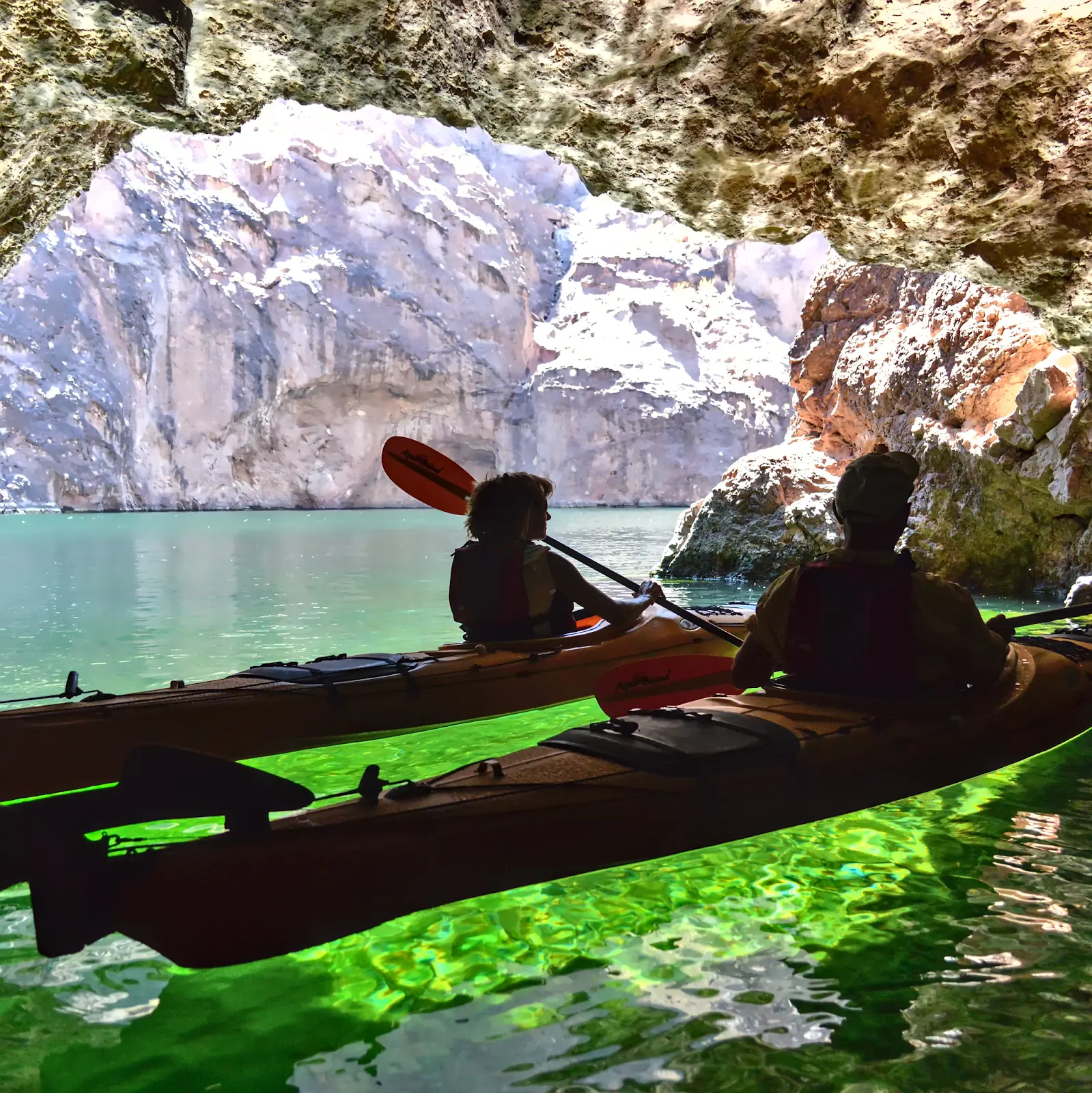 Kayakers inside Emerald Cave beside luminous green water