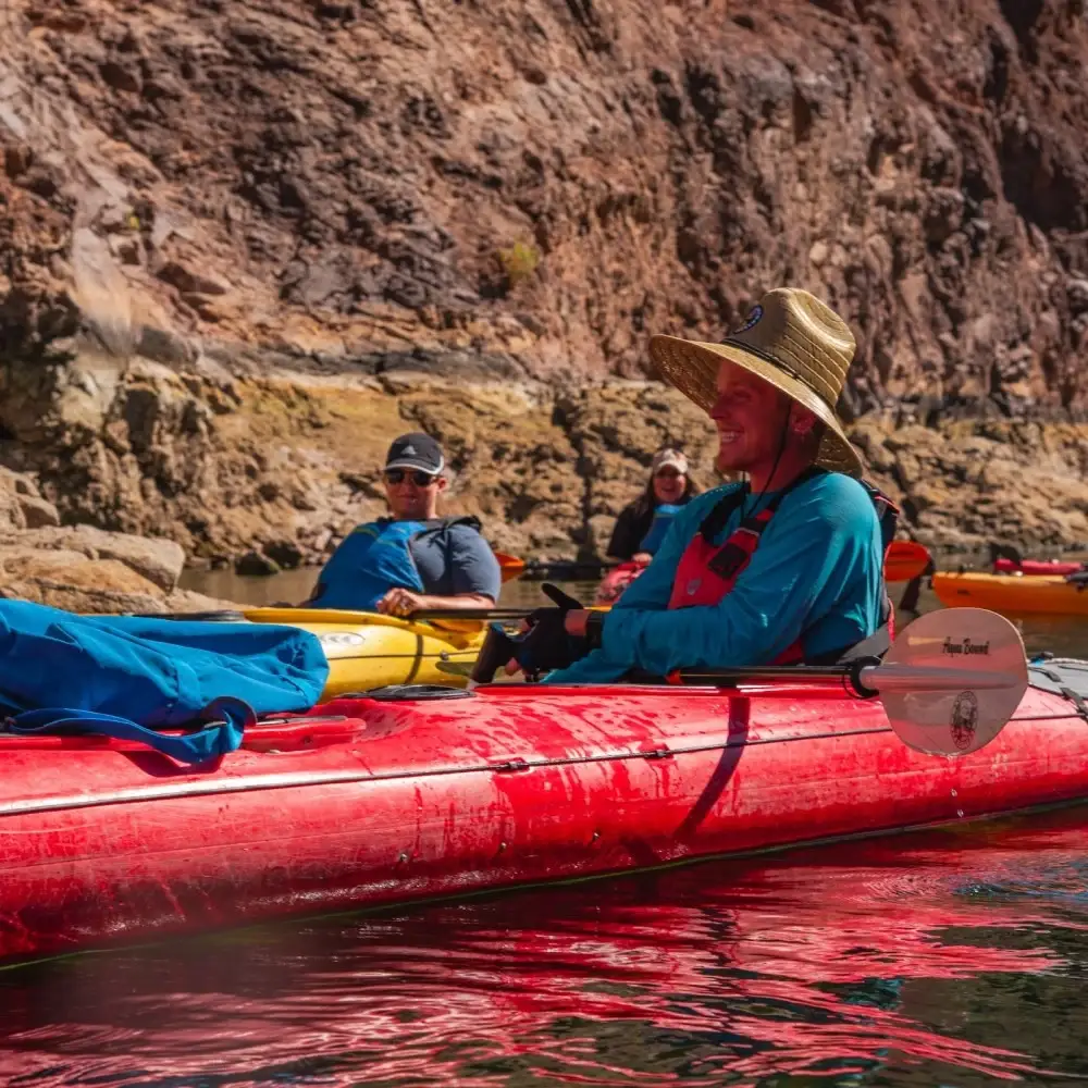 People kayaking on calm water beneath canyon cliffs