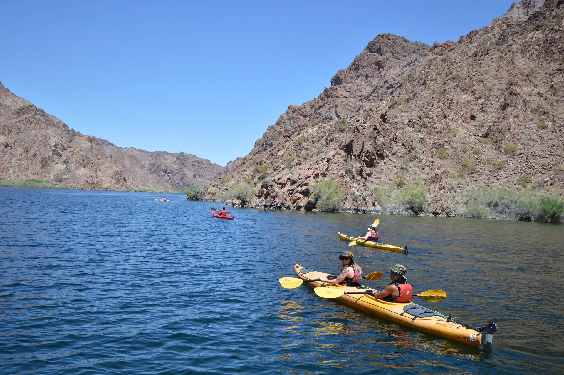 Kayakers paddling beneath golden canyon walls on the Colorado River